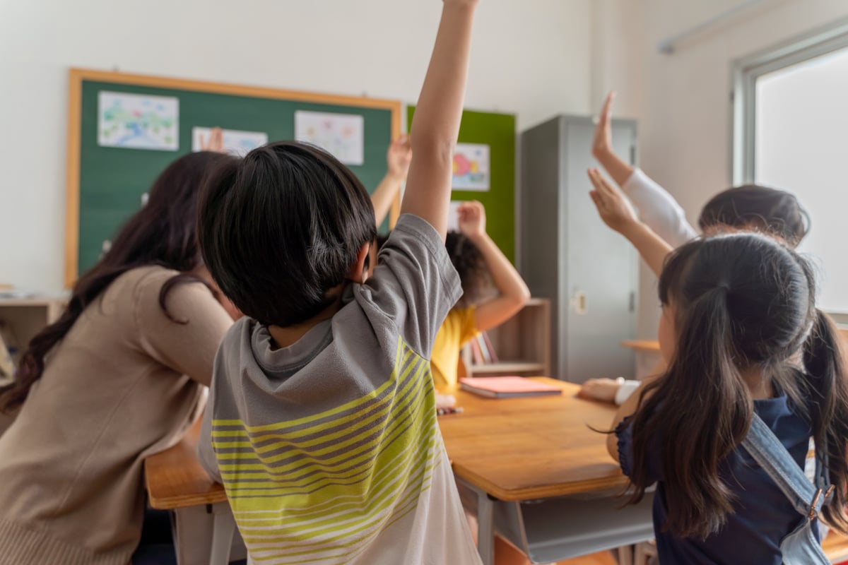 Asian School Teacher with Students Raising Hands